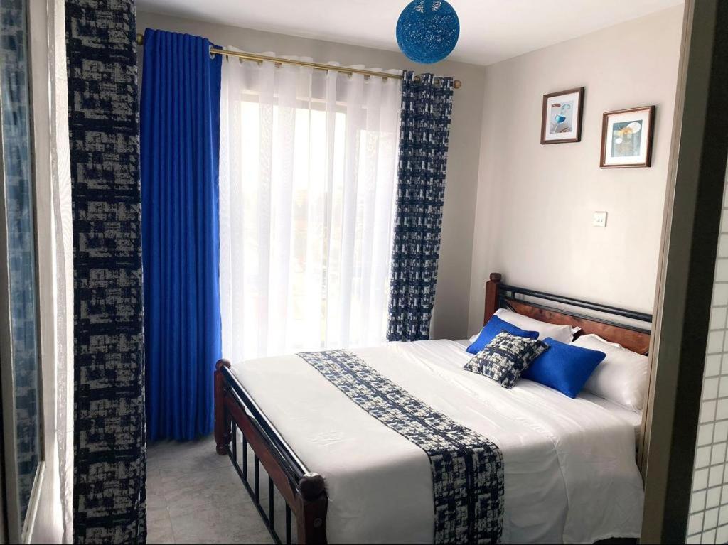 ein Schlafzimmer mit einem Bett mit blauen Vorhängen und einem Fenster in der Unterkunft Lux Suites Tsavo Studios Embakasi in Nairobi