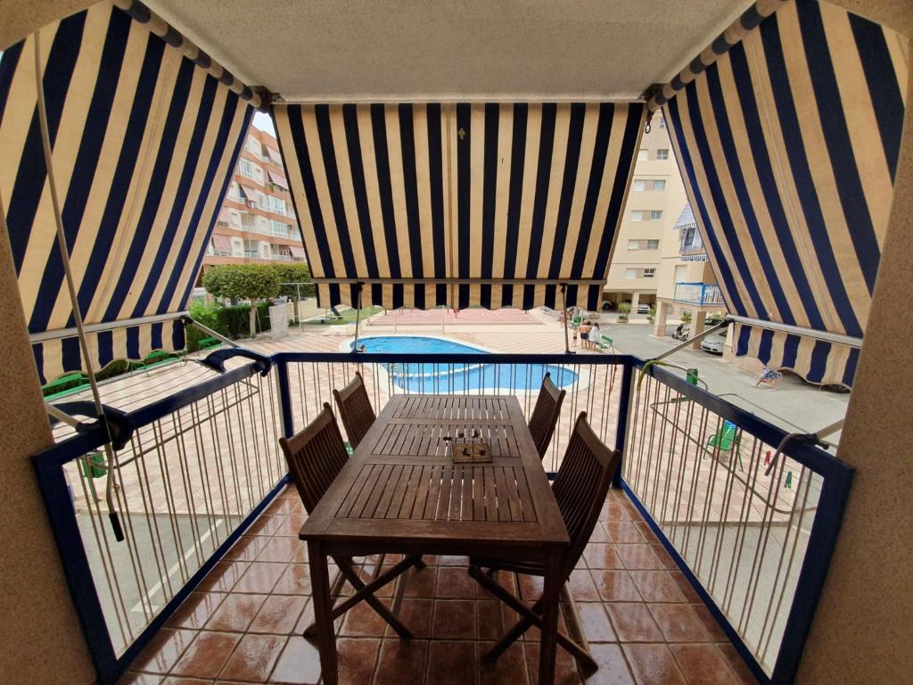 einen Balkon mit einem Holztisch, Stühlen und einem Pool in der Unterkunft Mediterraneo in Santa Pola