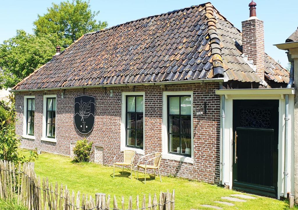 a brick house with a black door and a fence at Fakânsjehûs Sfeervol met fijne tuin in Irnsum