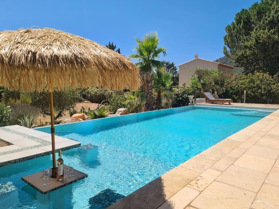 a swimming pool with a straw umbrella next to a house at Tiny House Roulotte in Cuges-les-Pins