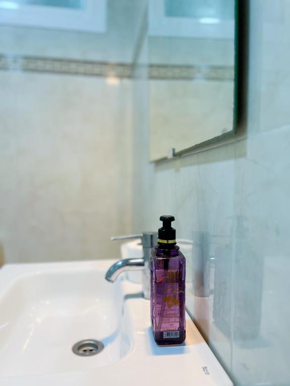 a purple bottle of soap sitting on a bathroom sink at Rif Appartment in Al Hoceïma