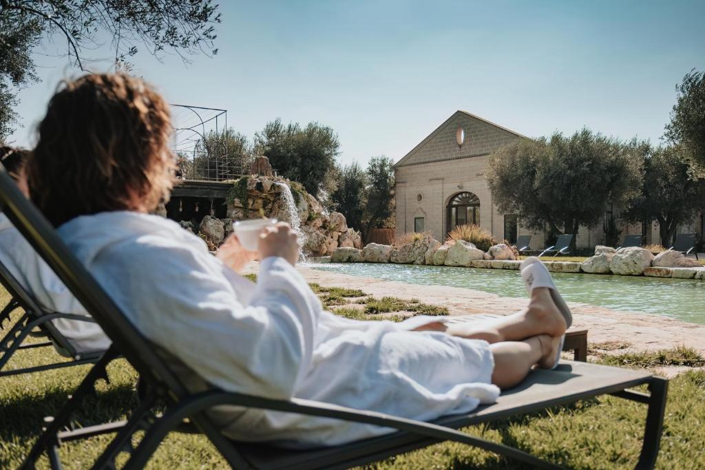 une femme assise sur une chaise devant une fontaine dans l'établissement Masseria Le Lamie, à Villa Castelli