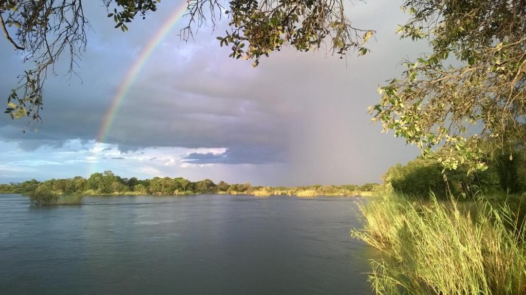 um arco-íris no céu sobre um rio em Mobola Lodge em Mamono
