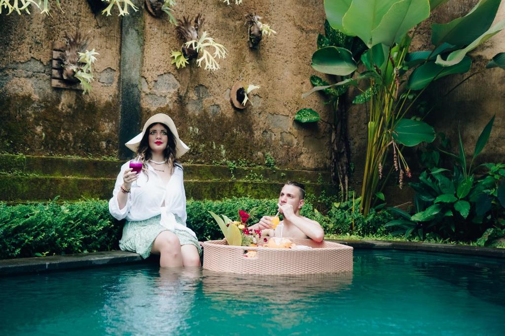 a man and a woman sitting in a swimming pool at The Alus Cottage and Villa in Ubud