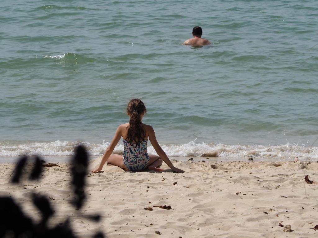 a woman sitting on the beach with a man in the water at Anyavee Tubkaek Beach Resort in Tab Kaek Beach