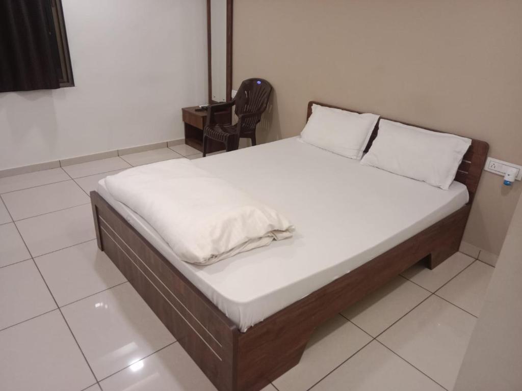 a bed with white sheets and a chair in a room at Hotel Shreeji's in Gandhinagar