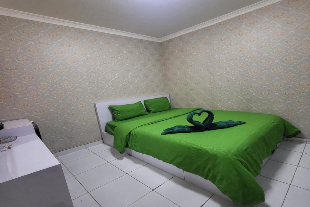 a bedroom with a green bed with a black ribbon on it at B Nature Aeropolis Inn in Teko