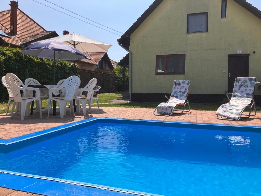 uma piscina com cadeiras, uma mesa e um guarda-sol em Lellei Pihenőház Balatonlelle em Balatonlelle
