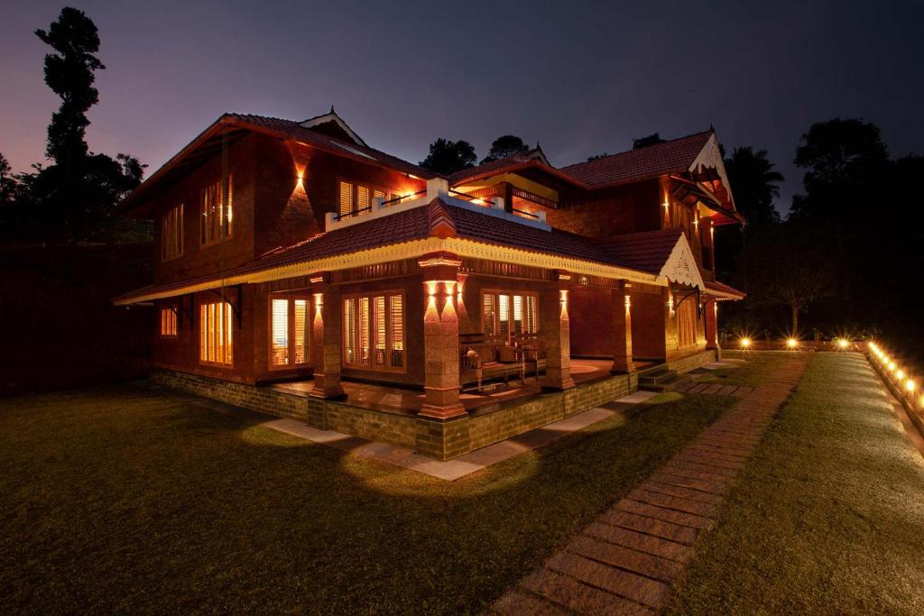 a large wooden house at night with lights at Regal Retreat by VEO - Part of StayVista in Wayanad