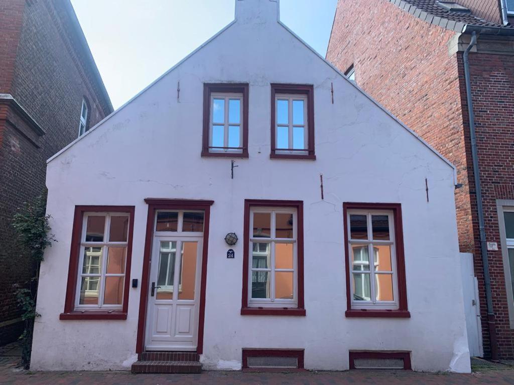 a white house with red windows and a door at Kaptainshuus Apartment A in Leer