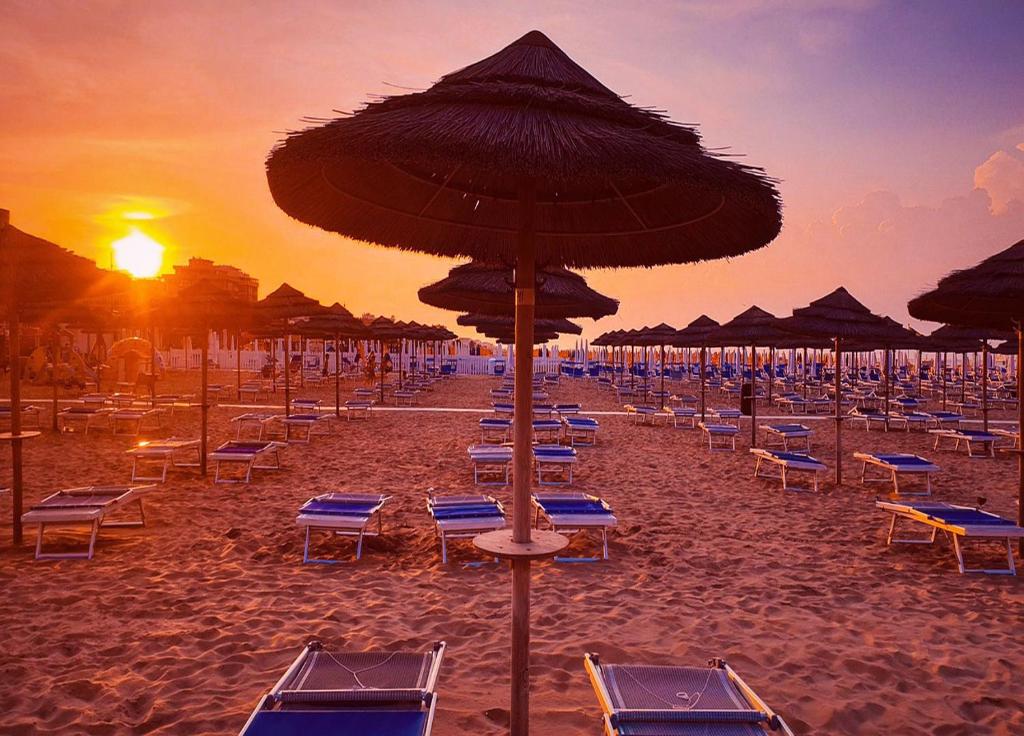 a beach with chairs and umbrellas at sunset at Hotel Caesar in Misano Adriatico