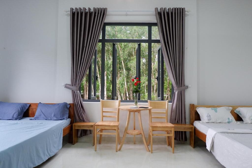 a room with two beds and a table with chairs and a window at Hương Tràm in Hồ Ðá