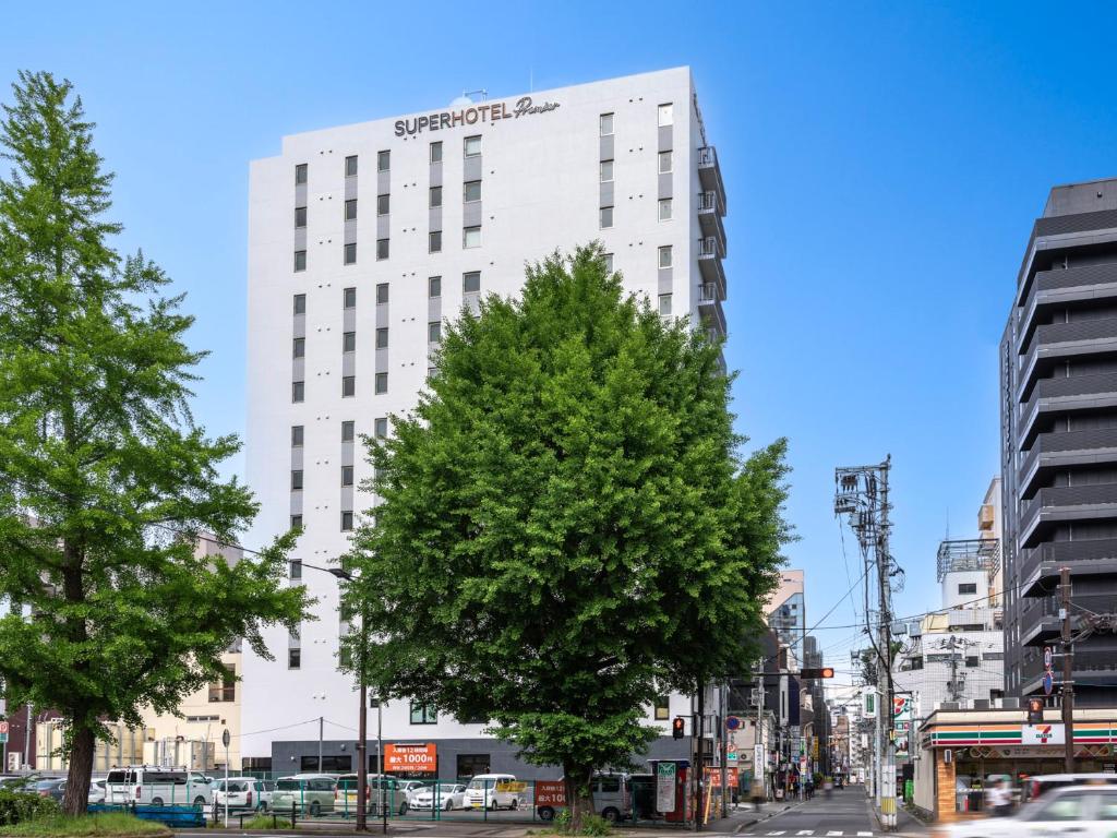 Super Hotel Premier Sendai Kokubuncho Tennenonsen في سيندايْ: مبنى ابيض طويل وامامه شجرة