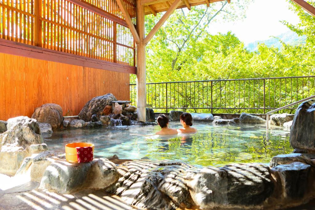 Ooedo Onsen Monogatari Hotel Kinugawa Gyoen في نيكو: شخصان في حوض استحمام ساخن في الفناء الخلفي