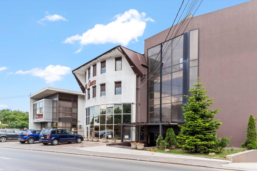 a building on a street with cars parked in a parking lot at Hotel Charter Otopeni in Otopeni