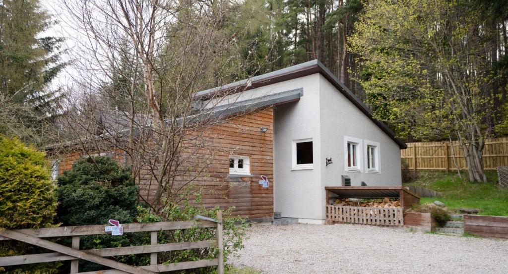 un petit bâtiment blanc et marron avec une clôture dans l'établissement Salmon Run Lodge, à Carrbridge