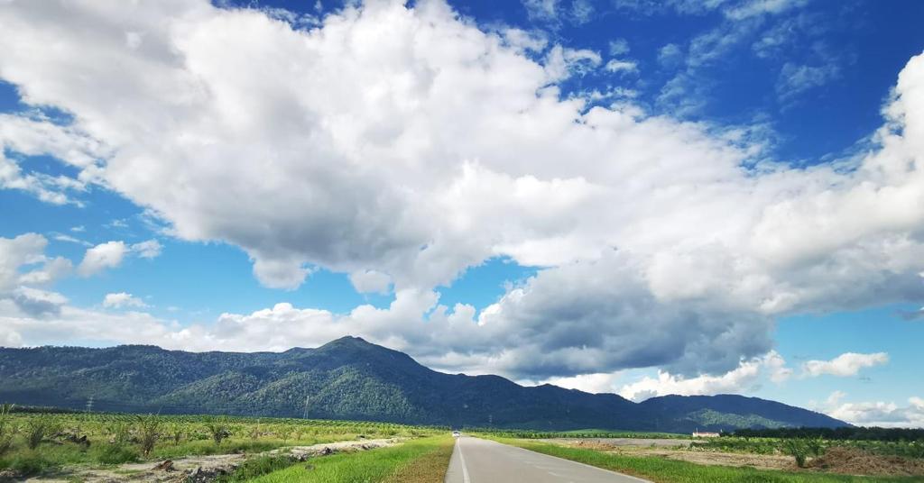 an empty road with a cloudy sky and mountains at Spacious Room in Gunung Ledang 