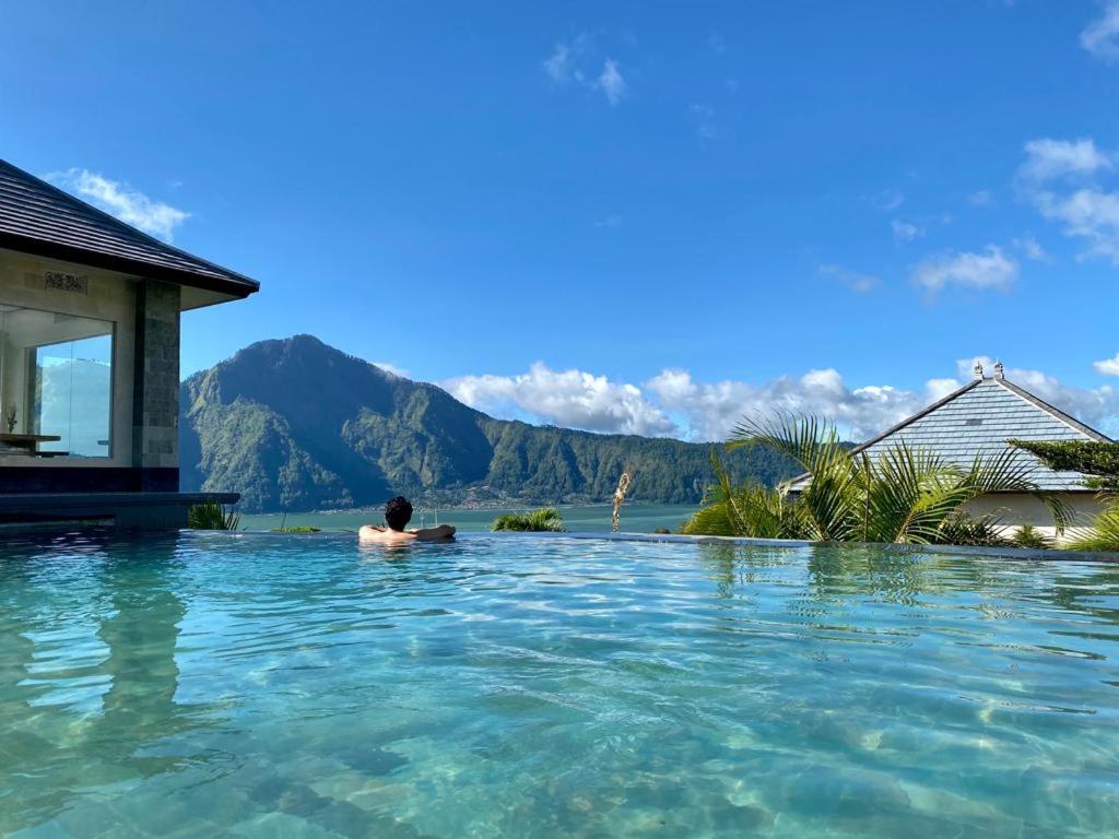 un homme dans une piscine avec des montagnes en arrière-plan dans l'établissement Batur Green Hill, à Kintamani