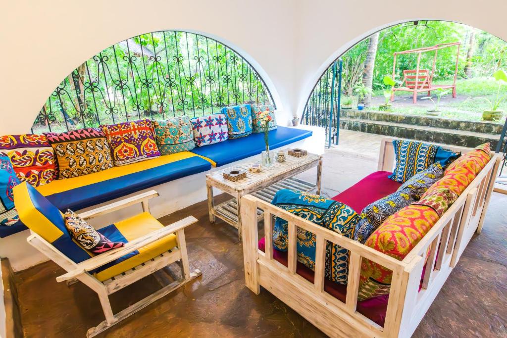 een woonkamer met een bank, stoelen en ramen bij Footprints House in Diani Beach