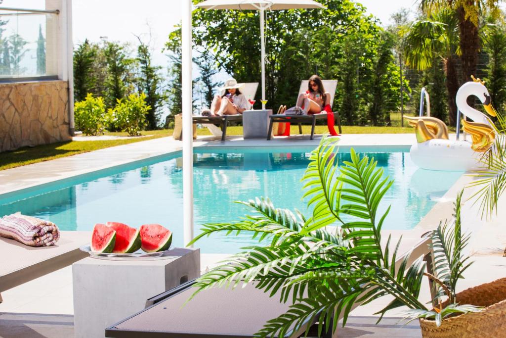 una piscina con due persone sedute su sedie e cocomeri accanto ad essa di Grande Terra Villas with Swimming Pool a Spartýlas