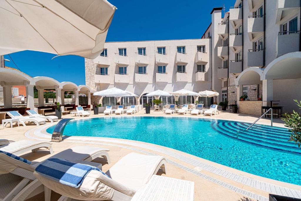 a swimming pool with chairs and umbrellas next to a building at Hotel Korkyra in Vela Luka