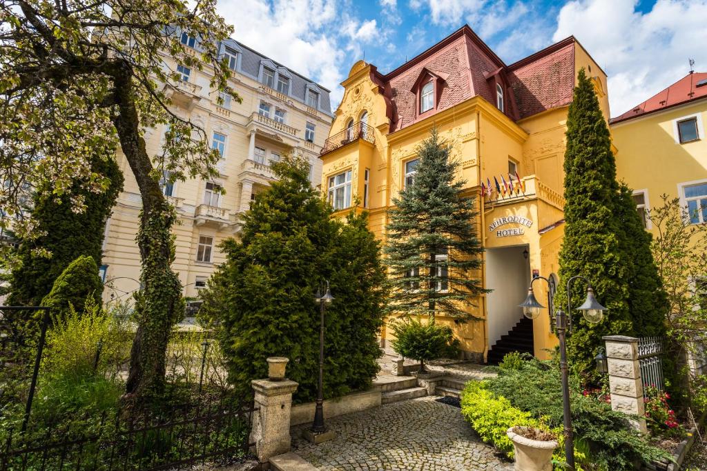 瑪麗亞溫泉的住宿－Aphrodite Hotel Marianske Lazne，前面有树木的黄色房子