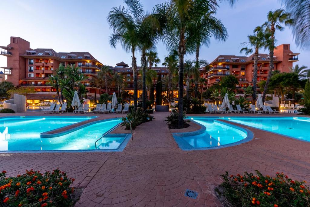 a pool at a resort with palm trees and buildings at Puerto Antilla Grand Hotel in Islantilla