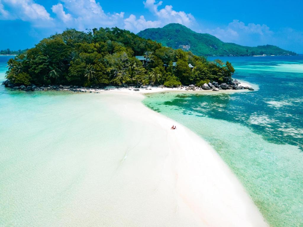 JA Enchanted Island Resort Seychelles في Round Island: جزيرة في المحيط مع شخص على الشاطئ