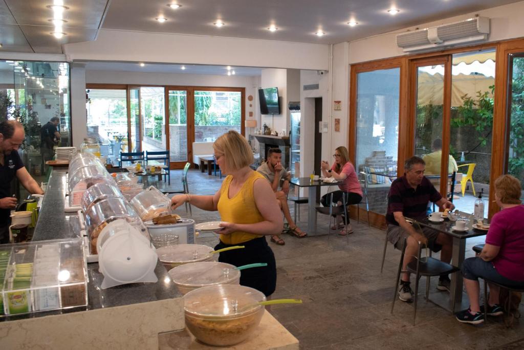 a woman preparing food in a kitchen with people sitting at tables at Stefanakis Hotel & Apartments in Varkiza