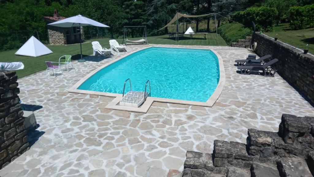 una piscina con sillas, una mesa y una sombrilla en appartamento con piscina tra la colline, en San Cristoforo