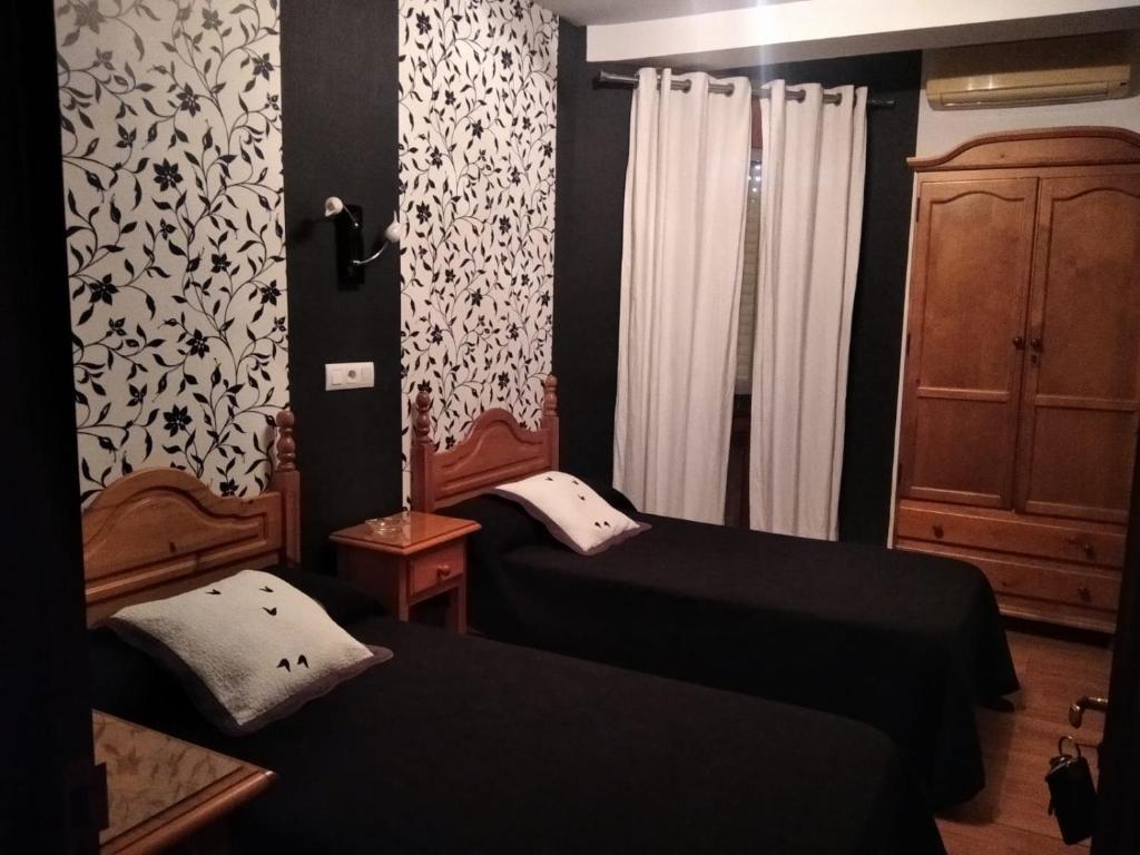 um quarto com duas camas e um armário e cortinas em Restaurante & Hostal El Volante em Moraleja