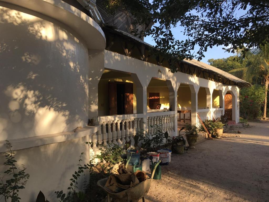 ein weißes Gebäude mit einer Veranda und einigen Pflanzen in der Unterkunft Karamba Lodge in Kafountine