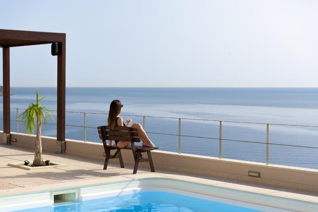 a woman sitting in a chair next to a swimming pool at Manificus Villas, Designed for Togetherness, By ThinkVilla in Palaiokastro