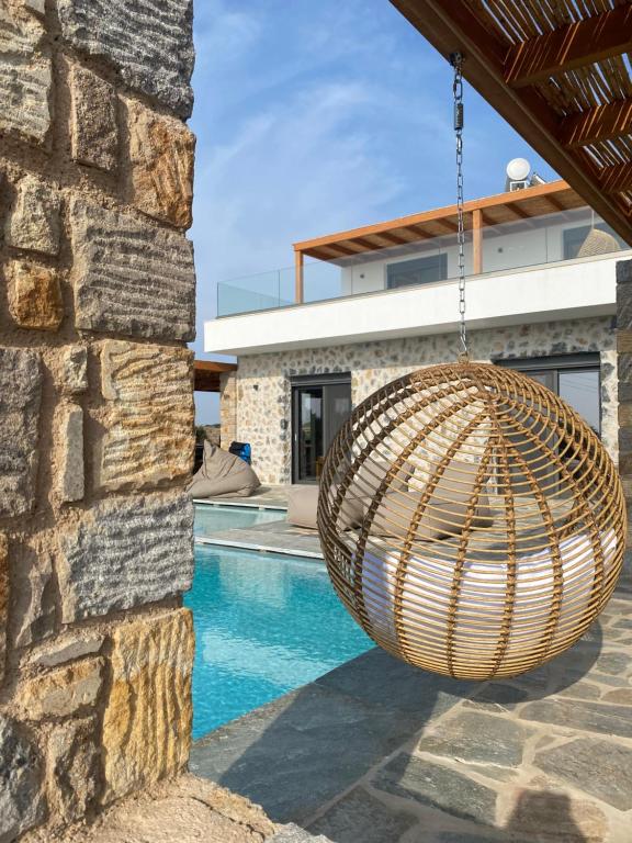 a wicker swing hanging from a stone wall next to a swimming pool at Villa Milan 1 mit Padelplatz in Kos Town