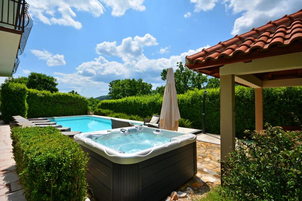 a hot tub in a yard with an umbrella at Villa Bisko with heated pool & jacuzzi in Trilj