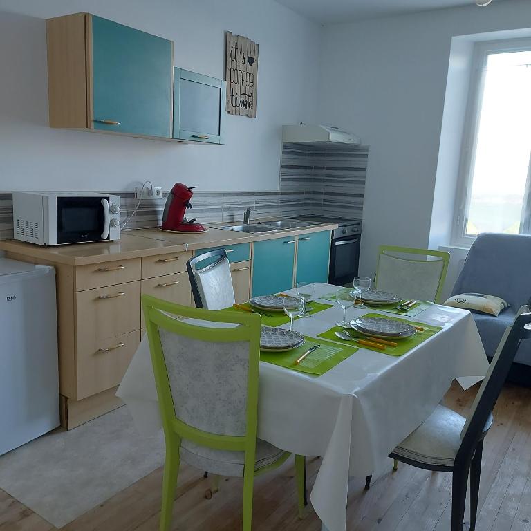 una cocina con mesa, mantel blanco y sillas verdes en Charmant appartement proche Carcassonne en Montgradail
