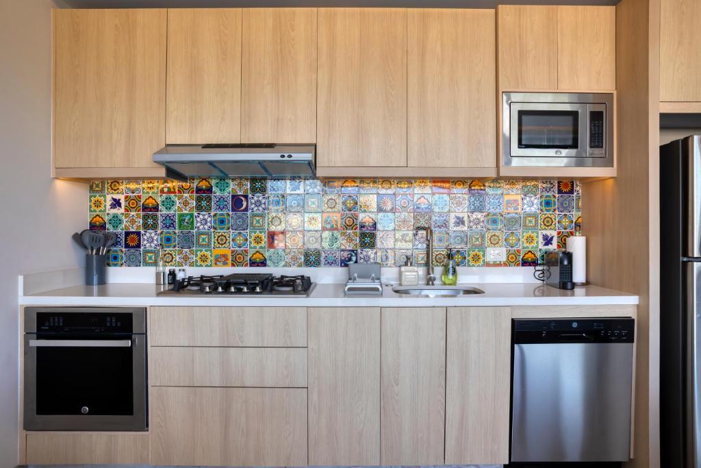 a kitchen with wooden cabinets and a tile wall at Lumina at Cardinal San José del Cabo in San José del Cabo