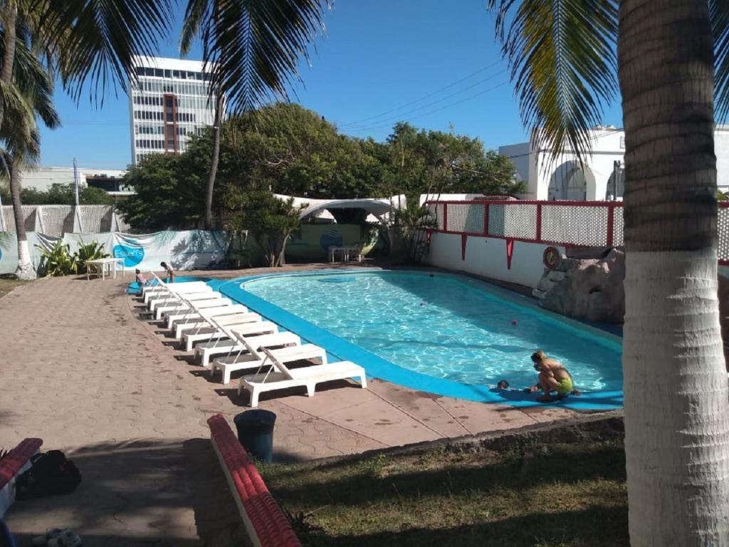 a swimming pool with lounge chairs and a person in the water at Hotel Essen's in Mazatlán