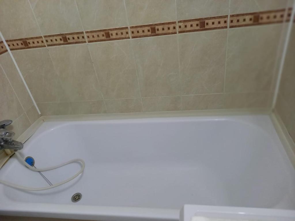eine weiße Badewanne mit einem Schlauch im Bad in der Unterkunft ОРАНЖЕВЫЙ МИР in Aqtöbe