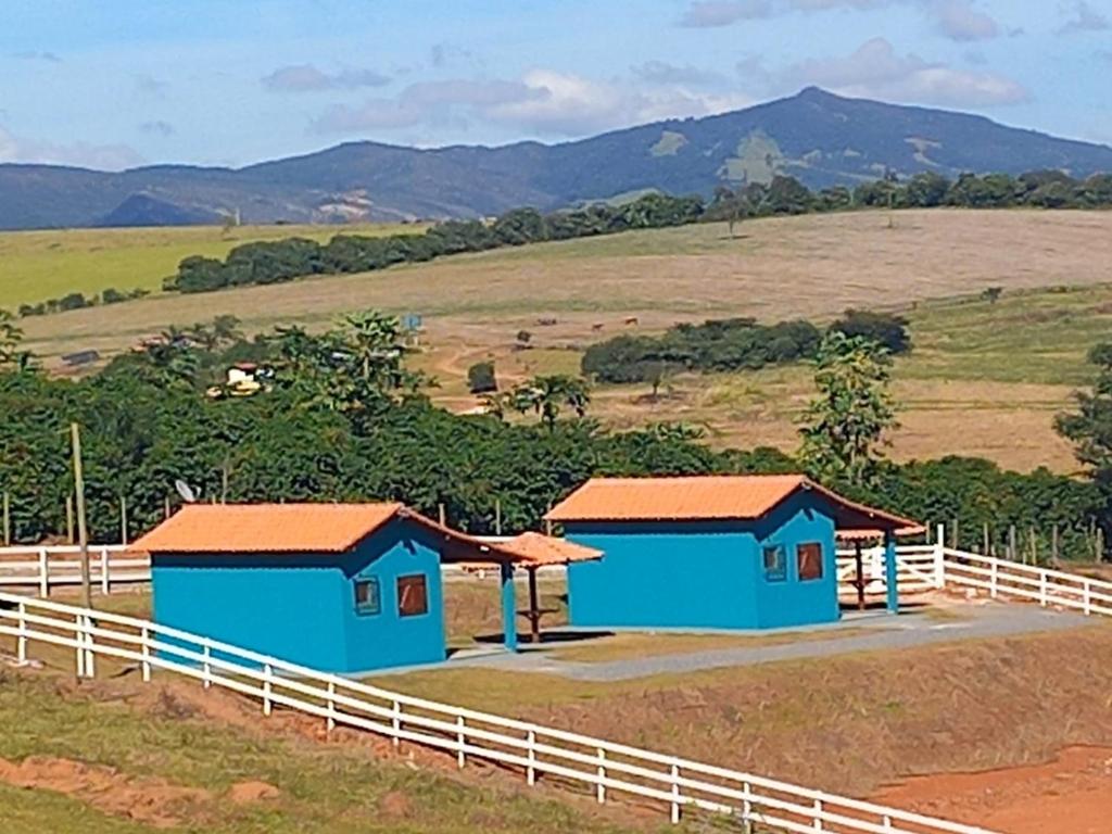 two blue buildings in a field next to a fence at Chales Horizonte das Pedras in São Thomé das Letras