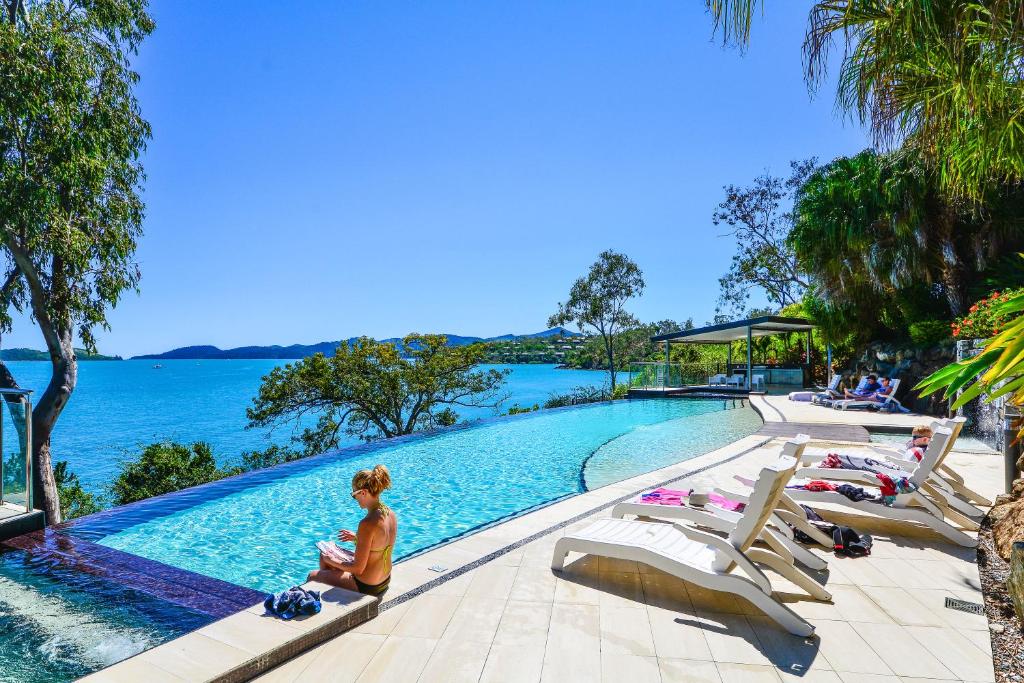 a woman sitting next to a swimming pool next to the water at Edge Waterfront Apartments in Hamilton Island