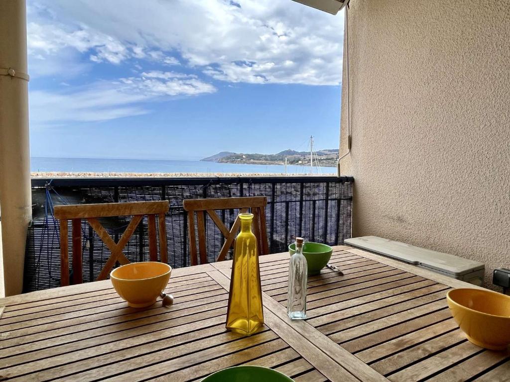 une table en bois avec des bols et une bouteille sur un balcon dans l'établissement Studio 4 pers, 150m Mer, Clim, Terrasse, Parking, Ascenseur - Argelès-sur-Mer - FR-1-225-783, à Argelès-sur-Mer