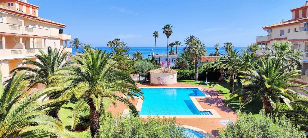 a swimming pool with palm trees in front of a building at Apartamento La Marina by DENIA COSTA in Denia