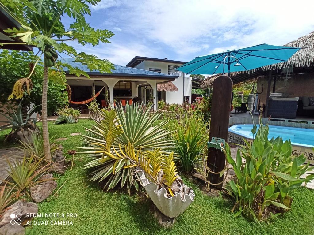 um quintal com piscina e uma casa com guarda-sol em La Maison Du Voyage em Tevaitoa