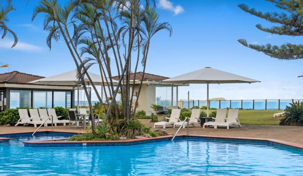 - une piscine avec des chaises longues et des parasols à côté d'un complexe dans l'établissement Nautilus Resort Apartment 162 Solitary Islands Way 8, à Sapphire Beach