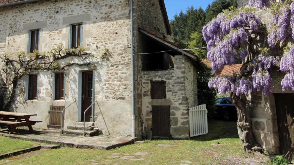 uma velha casa de pedra com uma árvore roxa ao lado em Les Points Cardinaud em Saint-Laurent-les-Églises