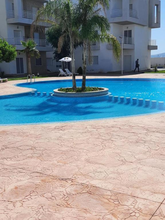 a blue swimming pool with a palm tree in front of a building at appartement résidence Palm Beach Saidia in Oujda