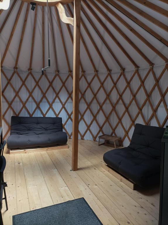 Spacious yurt living area with two black futon sofas and central wooden support post.