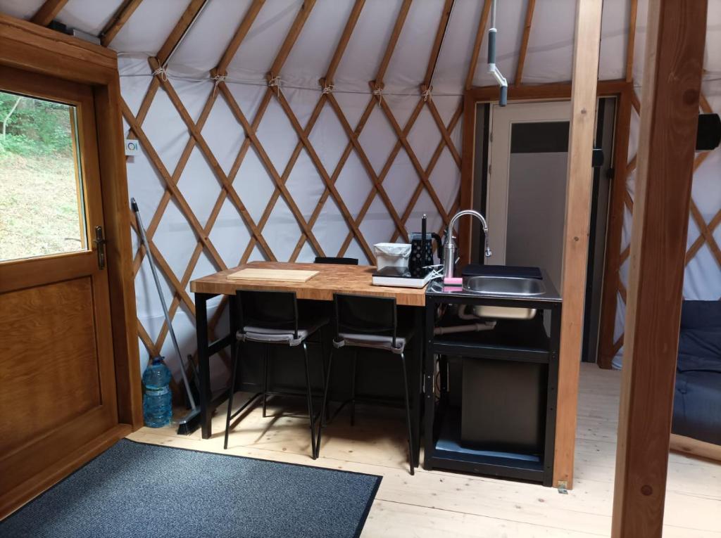 Compact yurt kitchenette with wooden counter, sink, three bar stools and entrance door.