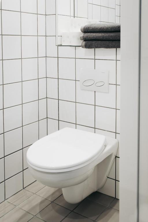 Wall-mounted white toilet against white tiled walls with neatly folded dark towels.